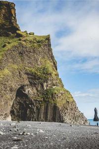 Photo of cliffside with cave mouth and next to a body of water.